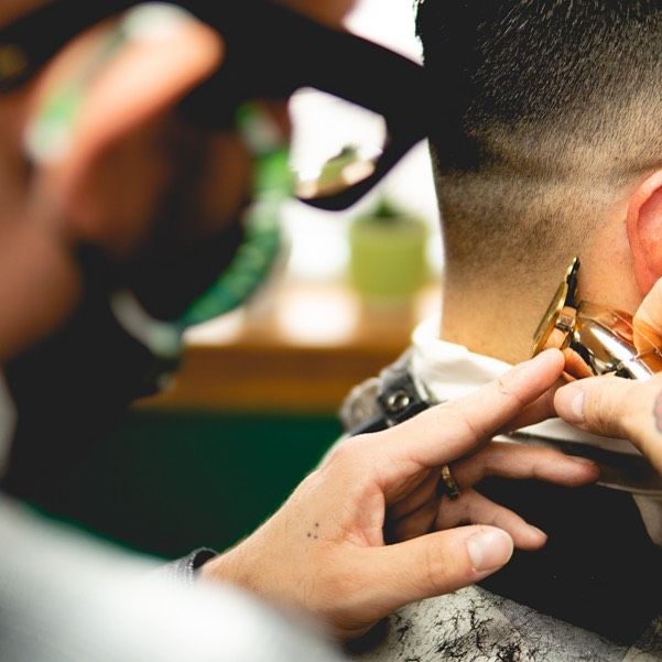 Close up photo of Jimmy Giroux, barber at Collective Haus tapering a client’s hair with a electric razor.